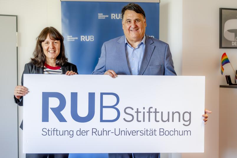 Porträt von Susanne Seiler und Martin Paul mit einem Schild mit der Aufschrift "RUB Stiftung"