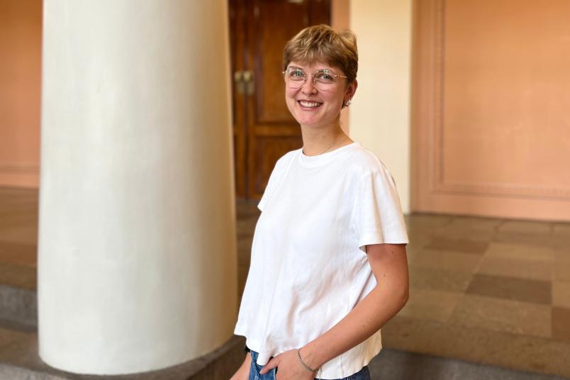 Eine junge Frau im weißen Shirt vor einer dicken Säule