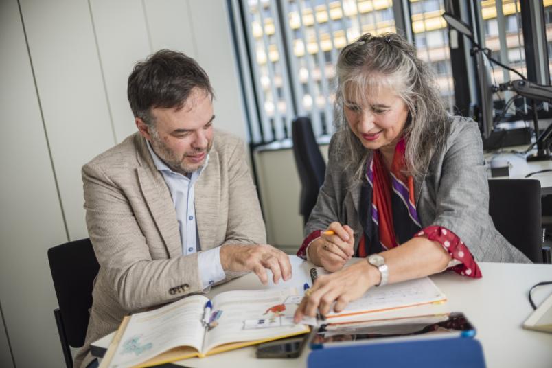 Björn Rothstein und Karin Yeşilada schauen mehrere Bücher und Unterrichtsmaterialien an.