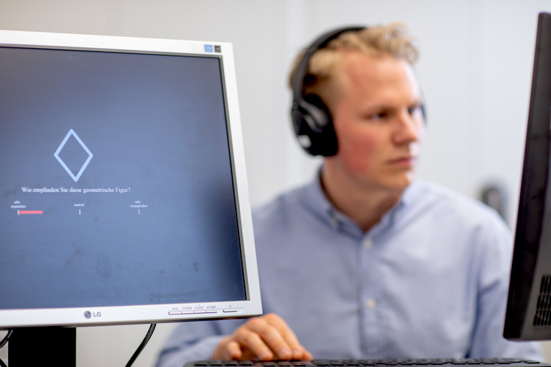 Ein Mann mit Kopfhörern arbeitet an einem Rechner, auf einem Monitor ist eine Raute zu sehen