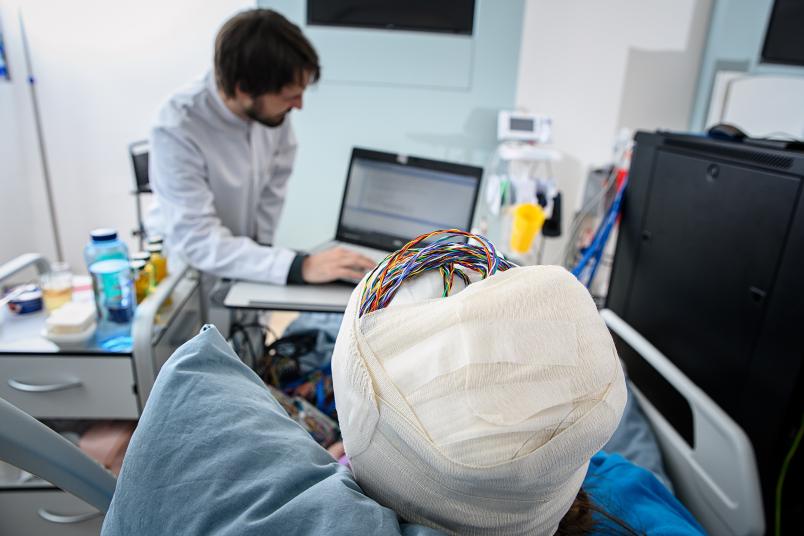Eine Person mit verbundenem Kopf, aus dem Verband schauen Kabel heraus. 