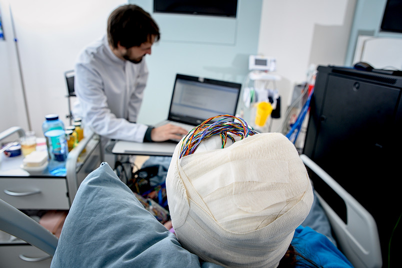 Eine Person mit verbundenem Kopf, aus dem Verband schauen Kabel heraus. 