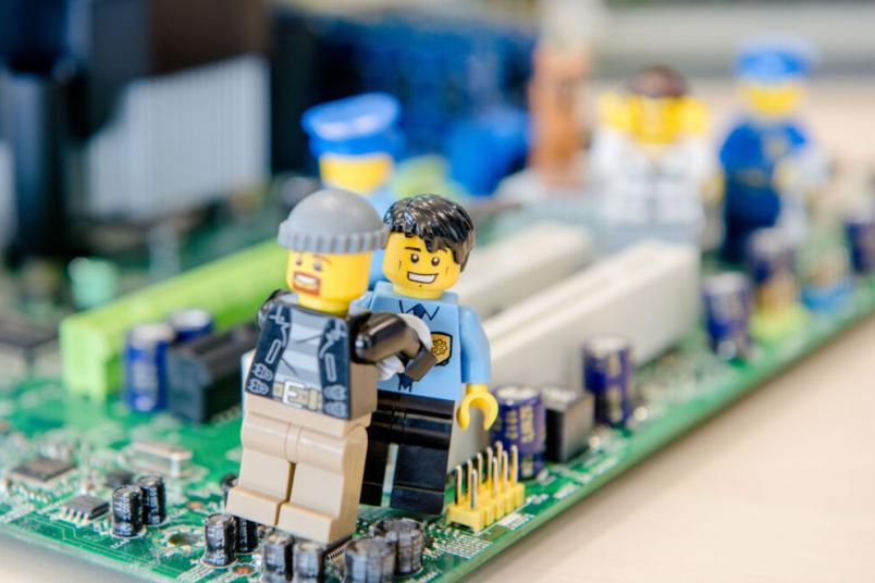 Ein Polizisten-Lego-Männchen nimmt ein Gauner-Lego-Männchen fest, während sie auf einer Computerplatine stehen.