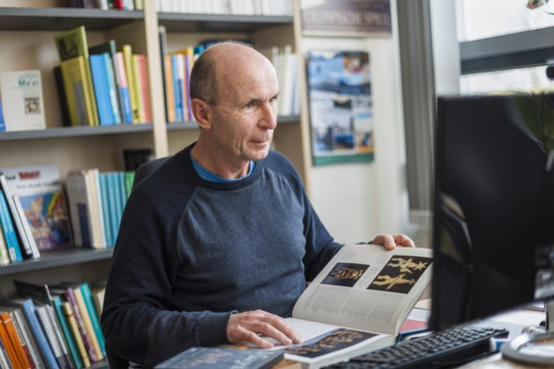 Eine Person arbeitet am Rechner, im Hintergrund viele Bücher