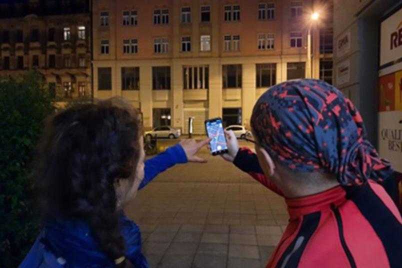 Zwei Personen von hinten, die mit einem Smartphone eine Straßenlaterne anpeilen