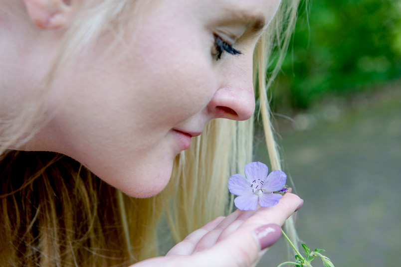 Eine junge Frau mit langen blonden Haaren riecht an einer lilanen Blume.