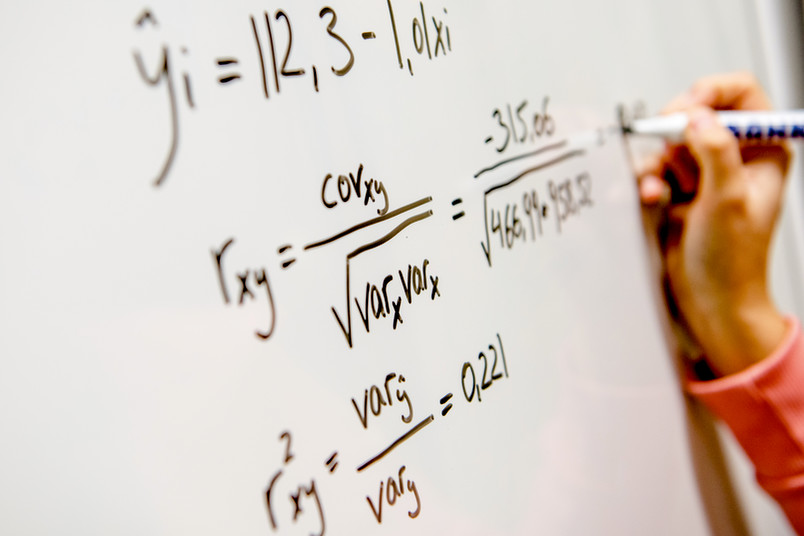 Hand schreibt Formeln an ein Whiteboard