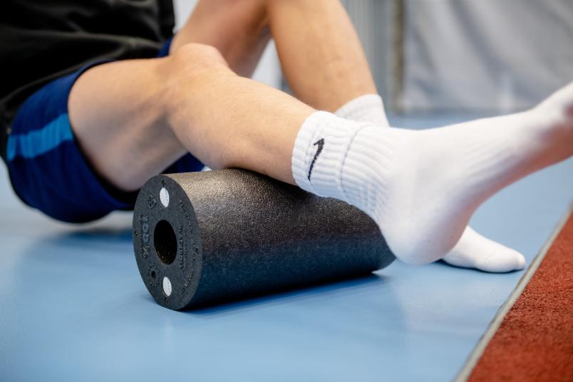 Sportler rollt Bein über eine Blackroll.