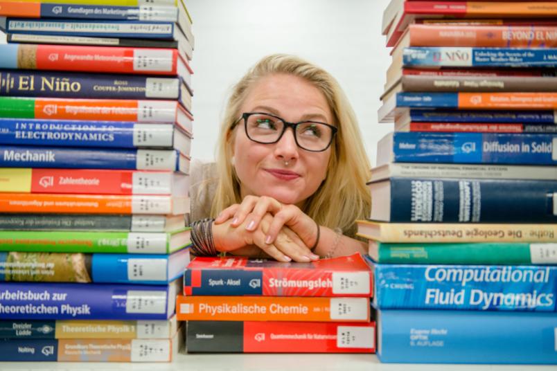 Studentin schaut durch einen Stapel Bücher. 