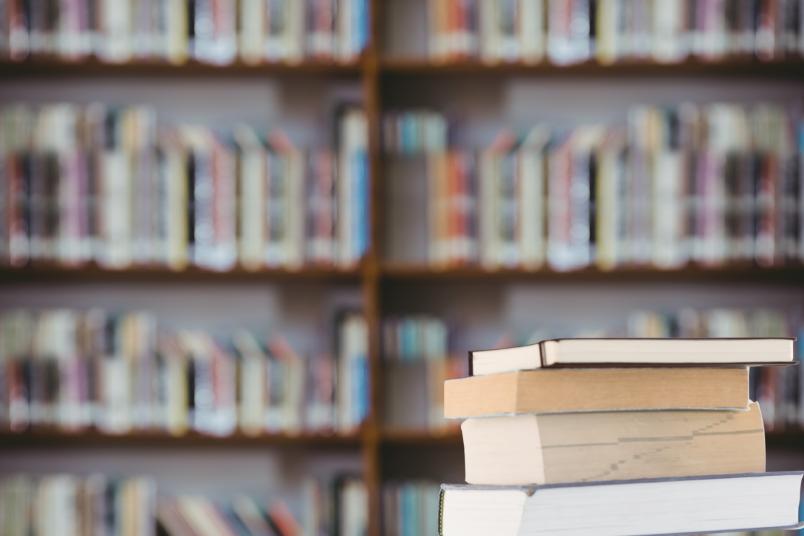 Ein Bücherstapel im Bildvordergrund vor einer Bücherwand