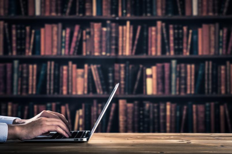 Mann am Laptop vor einer Bücherwand in der Bibliothek