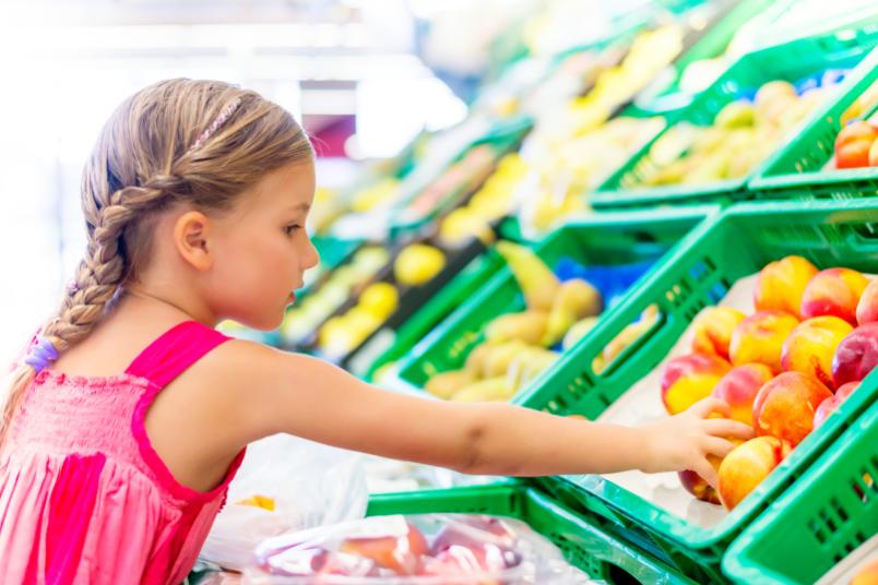Ein Mädchen greift im Supermarkt zu gesundem Obst.