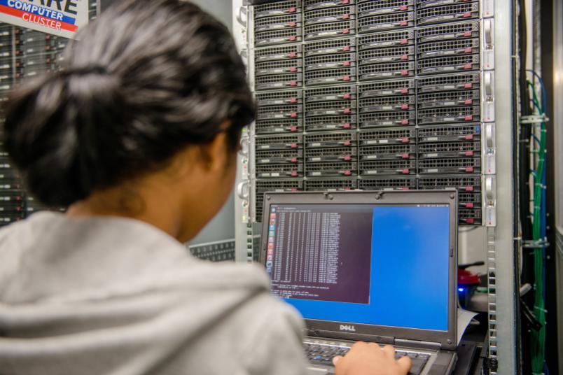 Person mit Laptop vor einem Rechencluster