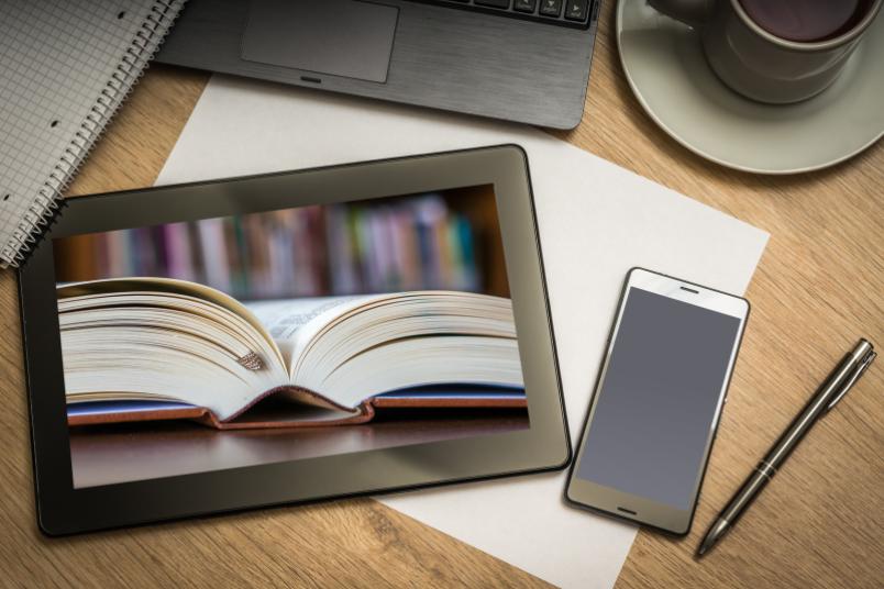 Ein aufgeschlagenes Buch ist auf dem Bildschrim eines Tabletcomputers zu sehen.
