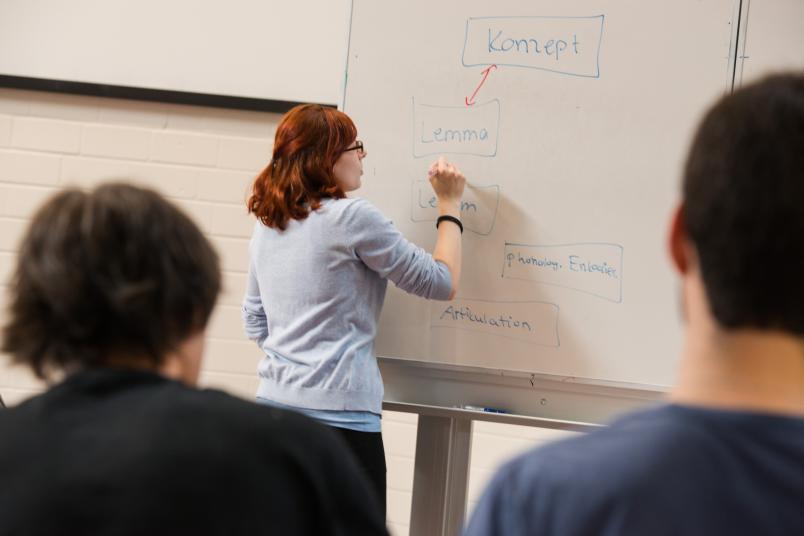Eine Studentin steht an der Tafel, zwei Studenten sehen ihr zu