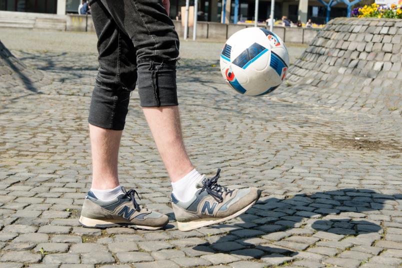 Mensch kickt Fußball in die Luft.