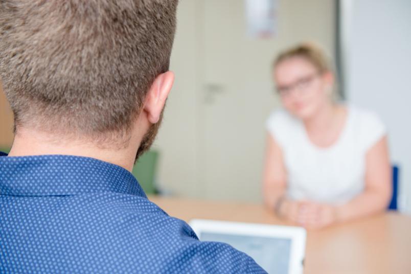 Zwei Menschen sitzen sich an einem Tisch gegenüber. Fotografiert über die Schulter der einen Person.