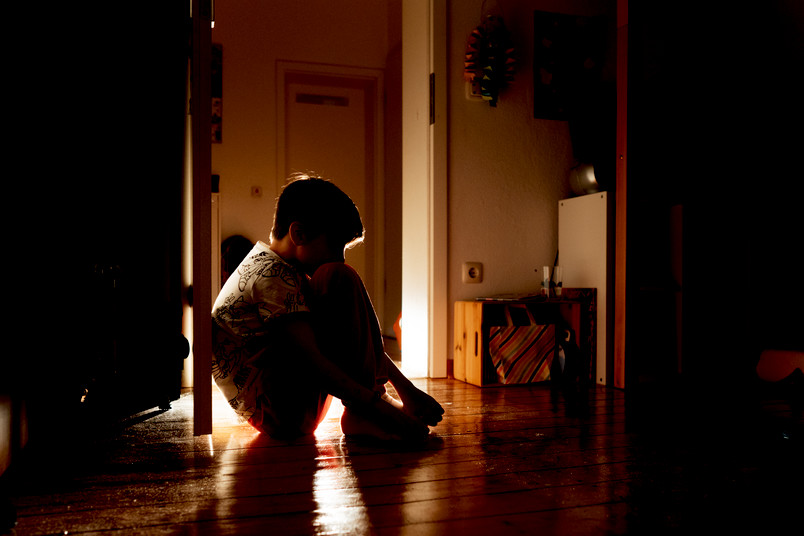 Ein Kind sitzt zusammengekauert in einem dunklen Zimmer.