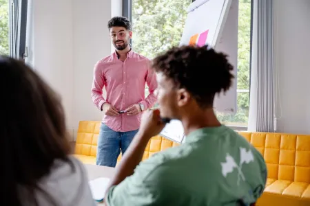 Lehrperson steht vor einem Flipchart. 