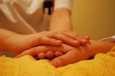 Eine Frau hält die auf einer Decke liegende Hand einer Person. 