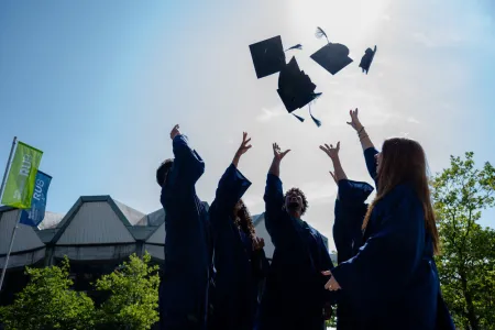 Studierende werfen Doktorhüte in die Luft. 