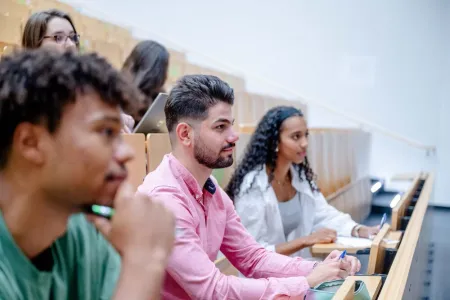 3 Studierende sitzen im Hörsaal der Ruhr-Universität Bochum. 