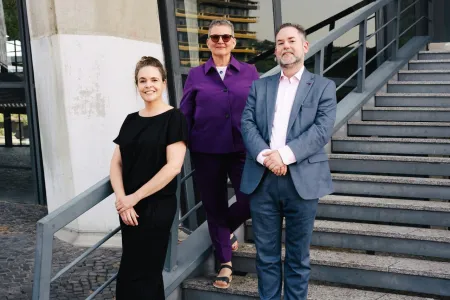 Zwei Wissenschaftlerinnen und ein Wissenschaftler stehen nebeneinander auf einer Treppe.
