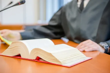 Ein Gesetzbuch liegt aufgeschlagen vor einer Person in Robe auf einem Tisch