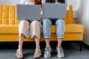 Studentinnen sitzen nebeneinander mit Laptops auf dem Schoß. 