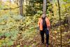 Ein Mann mit orangener Jacke steht im Laubwald.